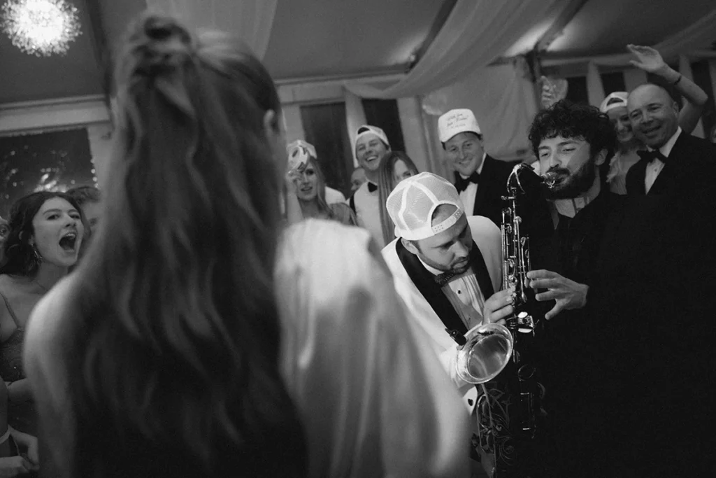 Documentary wedding photography, a candid, photojournalistic shot of a groom helping the saxophonist play on the dancefloor