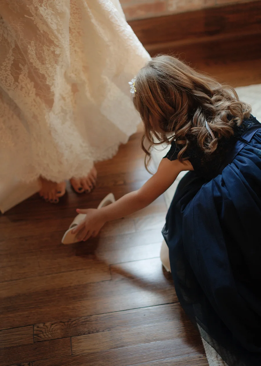 A strong example of documentary style wedding photography - a flower girl helps the bride with her shoes at a Houston, Texas wedding