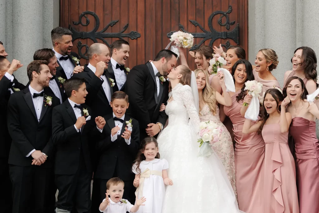 A newly married couple kiss outside the church surrounded by the bridal party