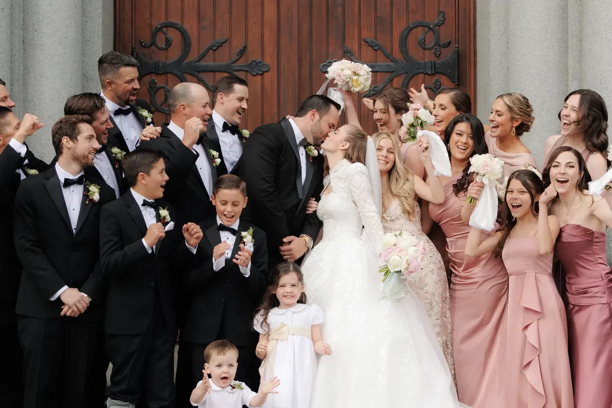 A newly married couple kiss outside the church surrounded by the bridal party