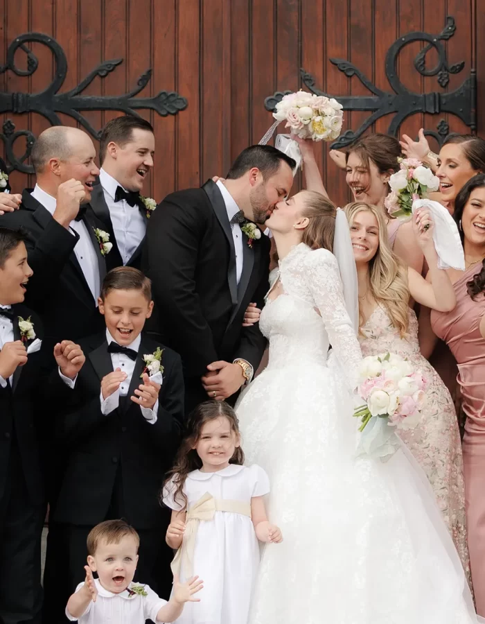 A newly married couple kiss outside the church surrounded by the bridal party