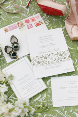 A flat lay detail shot of the invitation suite and personal items of the bride on the couples' custom print, including bride's shoes and florals