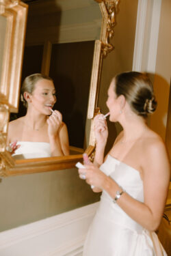 The bride applies lip gloss in the mirror